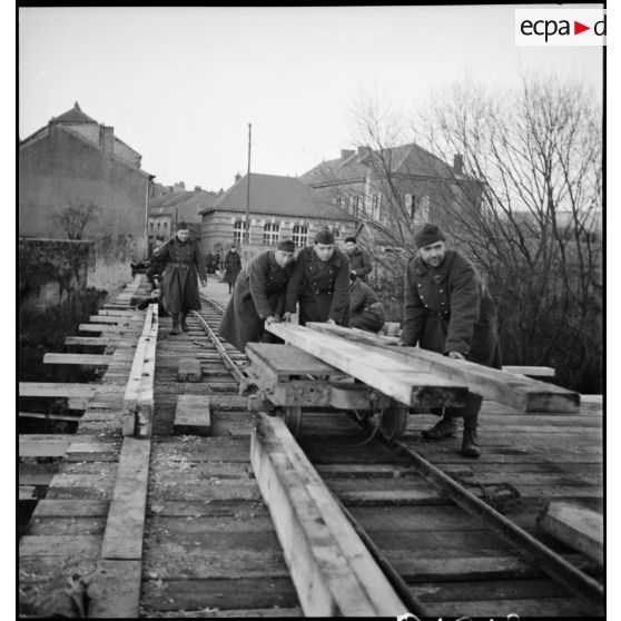 Des sapeurs du 6e RG poussent des poutres de bois sur le pont en construction qui enjambe la Meuse.