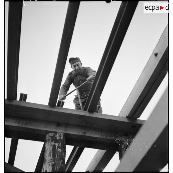 Un sapeur du 6e RG visse des écrous sur le pont en construction qui enjambe la Meuse.