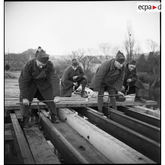 Des sapeurs du 6e RG vissent des écrous sur le pont en construction qui enjambe la Meuse.