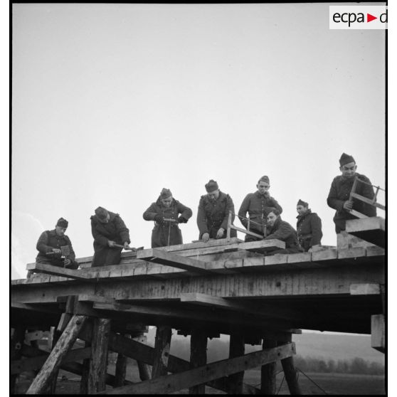 Des sapeurs du 6e RG vissent des écrous sur le pont en construction qui enjambe la Meuse.