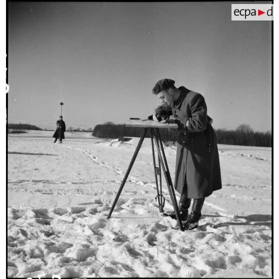 Dans un  paysage enneigé un lieutenant artilleur de la 2e armée relève un azimut sur une carte.