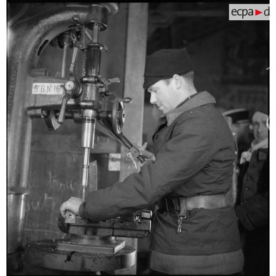 Plan américain de profil d'un soldat qui travaille sur une machine-outil.