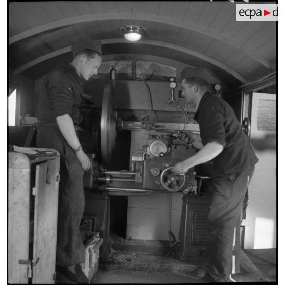 Deux mécaniciens travaillent sur une machine-outil dans une remorque de l'atelier de réparation de campagne.