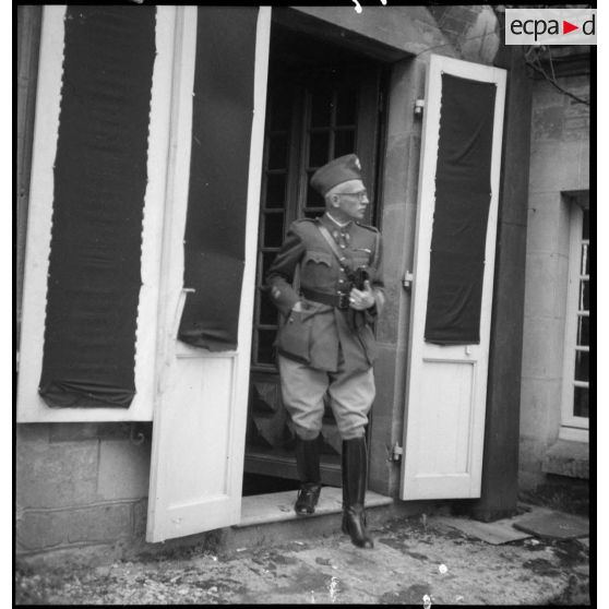 Un colonel est photographié en pied alors qu'il sort d'une maison par une porte-fenêtre.