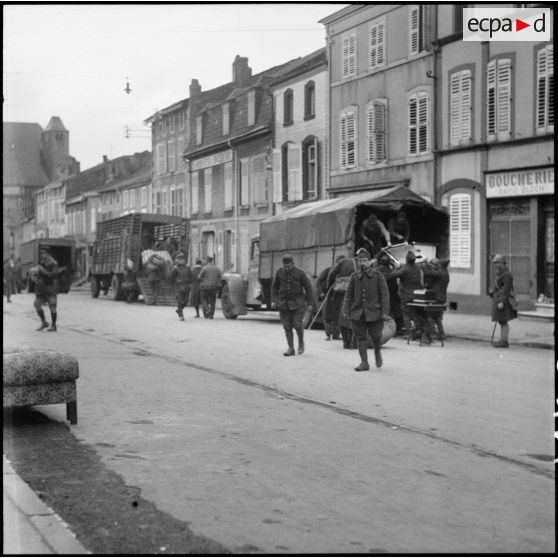 Plan général de soldats de la 3e armée qui chargent des camions dans une rue de village de la Moselle.
