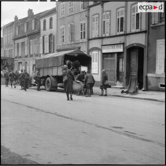 Plan général de soldats de la 3e armée qui chargent des camions dans une rue de village de la Moselle.