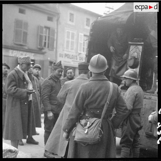 Des soldats de la 3e armée chargent un camion dans une rue de village de la Moselle. Un général les regarde.