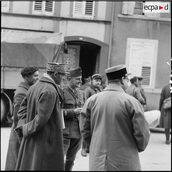 Des soldats de la 3e armée chargent un camion dans une rue de village de la Moselle. Un général les regarde.