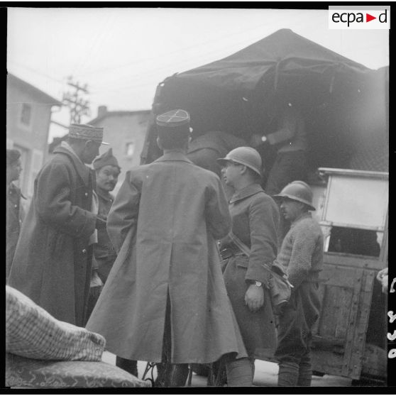 Des soldats de la 3e armée chargent un camion dans une rue de village de la Moselle. Un général les regarde.