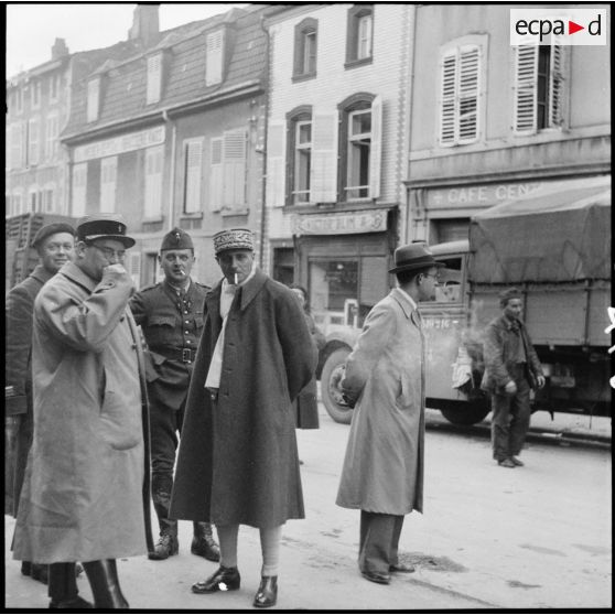 Des soldats de la 3e armée chargent un camion dans une rue de village de la Moselle. Un général les regarde.