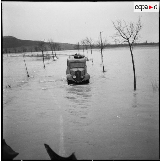 Une camionnette Peugeot de la 3e armée circule sur une route entièrement inondée.