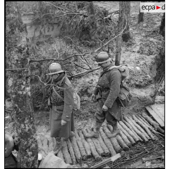 Des soldats marchent en colonne sur le sentier boueux d'une forêt dans le secteur de la 3e armée.