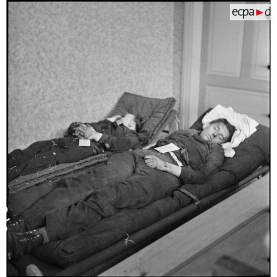 Plan général de deux cadavres de soldats de la 3e armée couchés sur des civières dans une pièce.