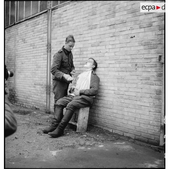 Dehors, un prisonnier allemand rase un de ses camarades.