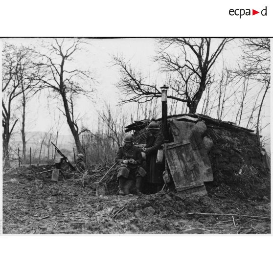 Deux soldats de la 4e armée se tiennent devant un abri de fortune, en arrière-plan une Hotchkiss M1914 sur affût berceau.
