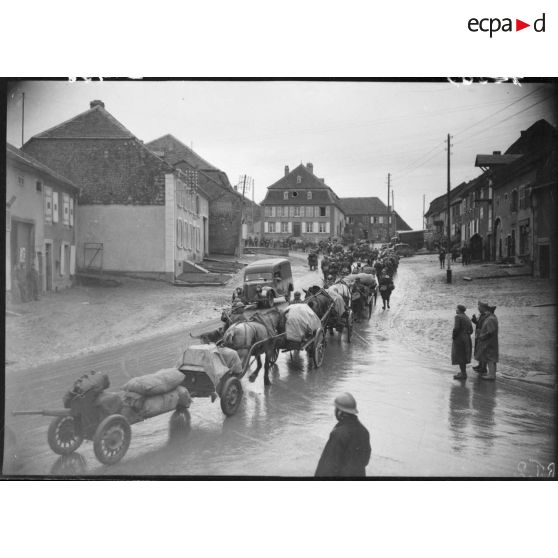 Un convoi hippomobile traverse un village.