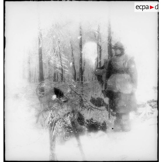 En forêt, un soldat de la 4e armée est photographié en pied près de toiles de tentes recouvertes de neige.