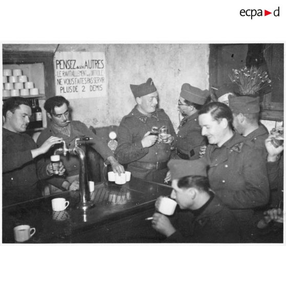Vue intérieur d'un foyer où des marsouins du 310e RAC boivent attablés à un bar.