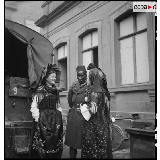 Un tirailleur sénégalais de la 5e armée est photographié entouré de deux alsaciennes en tenue traditionnelle.