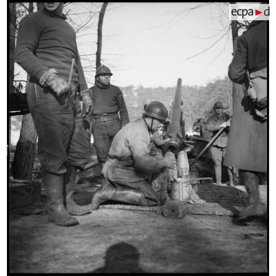 Un artilleur de la 5e armée à genoux s'occupe d'un obus, en arrière plan le 155 mm GPF est visible.