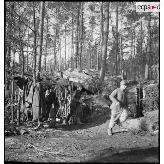 Dans un bois, des artilleurs de la 5e armée sortent en courant d'un abri de rondins.