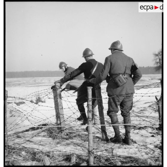 Lors d'une patrouille des soldats de la 5e armée enjambent des barbelés dans la neige.