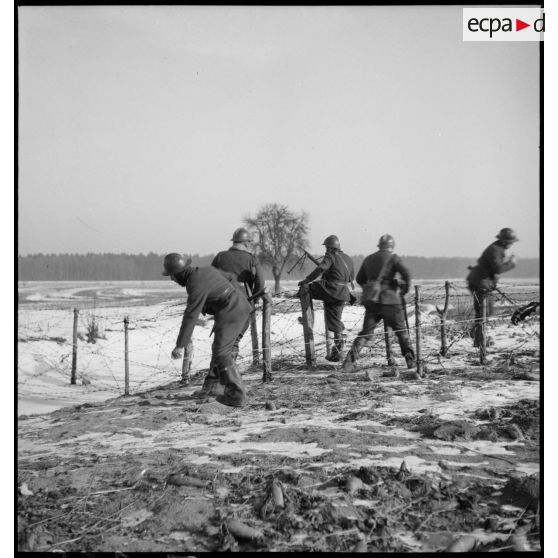 Lors d'une patrouille des soldats de la 5e armée enjambent des barbelés dans la neige.