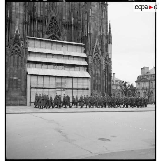 Des soldats de la 5e armée se déplacent en ordre serré devant le parvis de la cathédrale de Strasbourg, protégée contre les bombardements.