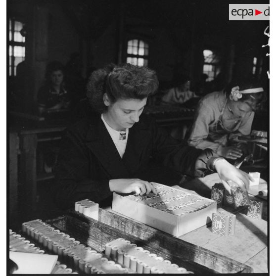 Dans un atelier une ouvrière travaille à la fabrication de piles électriques.