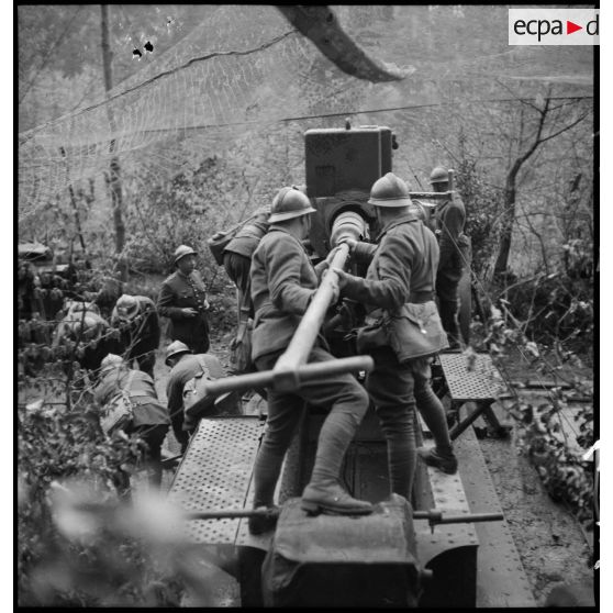 Des servants d'un  220 mm long M1917 donnent un coup de refouloir pour mettre une munition à poste.