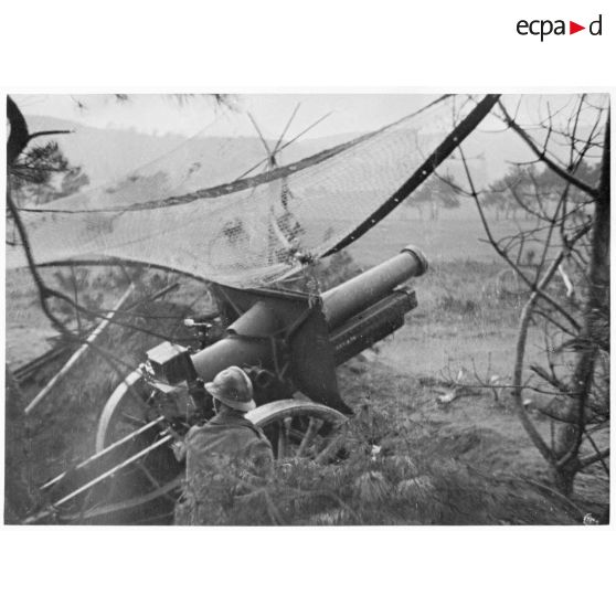 Tir d'une pièce de 155 mm court M1915/17. Cette dernière est photographiée en plan général de trois quarts dos.