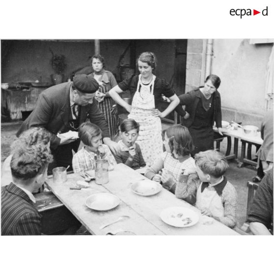 A l'extérieur dans une cour d'école, des enfants réfugiés mangent à table.