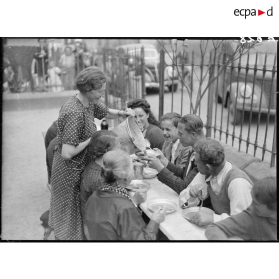 A l'extérieur dans une cour d'école, des enfants réfugiés mangent à table.