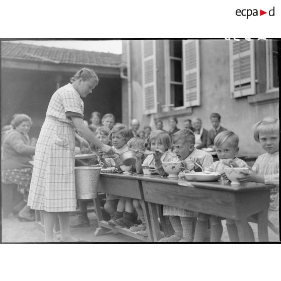 A l'extérieur dans une cour d'école, des enfants réfugiés mangent à table.