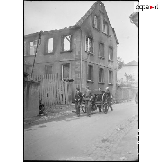 Des volontaires et un pompier tirent une pompe à bras près d'une maison calcinée dans un village.