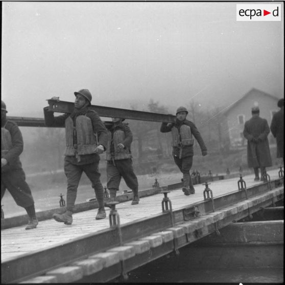 Des sapeurs du génie portent des traverses métalliques pour la construction d'un pont flottant.