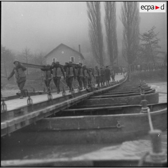 Des sapeurs du génie portent des traverses métalliques pour la construction d'un pont flottant.