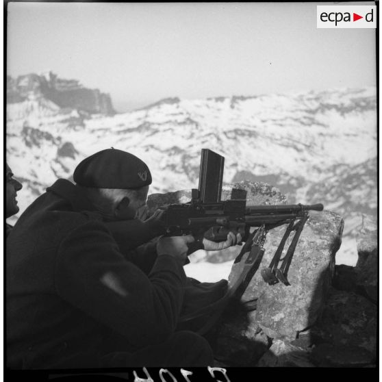 Un servant FM 24/29 du 86e BCA est posté dans un amas rocheux, il est photographié de dos.