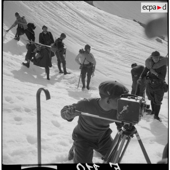 Un caméraman du SCA filme une scène alors que derrière lui des chasseurs du 86e BCA sont visibles.