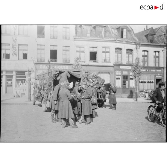 Des soldats de la 7e armée discutent devant des camions de transport de troupes camouflés, dans une rue commerçante d'un village.
