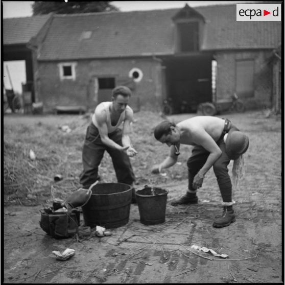 Des soldats de la 7e armée se lavent lors d'une halte dans la cour d'une ferme.
