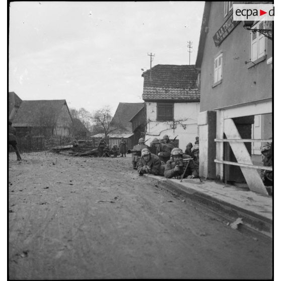 Des motocyclistes appartenant à une unité de cavalerie se mettent en position de tir à l'angle d'une maison.