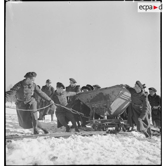 Des chasseurs alpins du 96e RIA tirent un chariot sur une voie de Decauville enneigée.