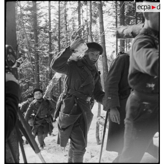 Dans une fôret enneigée, des soldats du 96e RIA transportent des troncs d'arbres qui viennent d'être abattus.