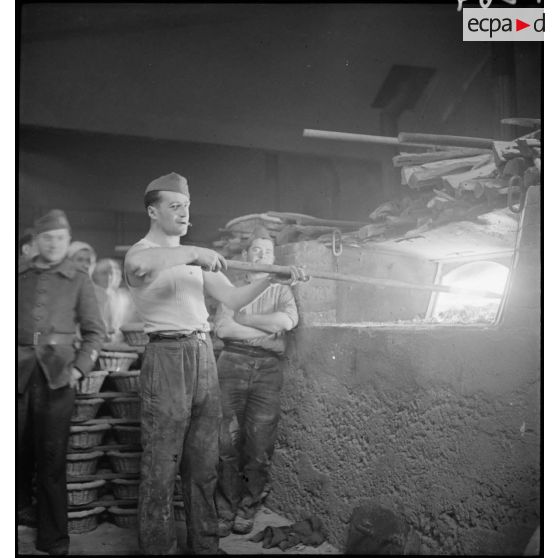 Un soldat enfourne un pain à l'aide d'une pelle de boulanger.