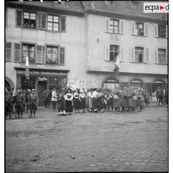 Soldats de la 8e armée et villageoises en costume traditionnel à Ribeauvillé, l'un des fantassins filme la scène.