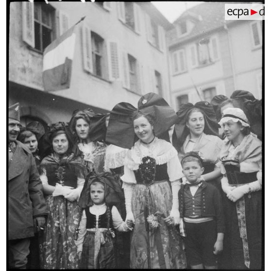 Soldats de la 8e armée et villageoises en costume traditionnel à Ribeauvillé, l'un des fantassins filme la scène.