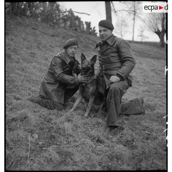 Deux soldats et leur chien, assis en marge d'une formation cynophile.