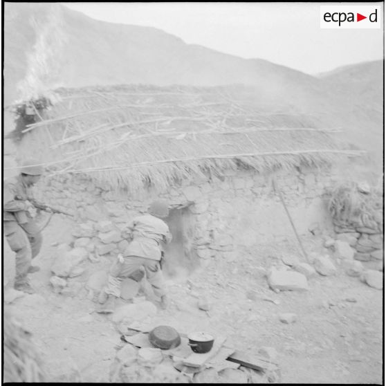 Des soldats se postent devant une habitation en feu.
