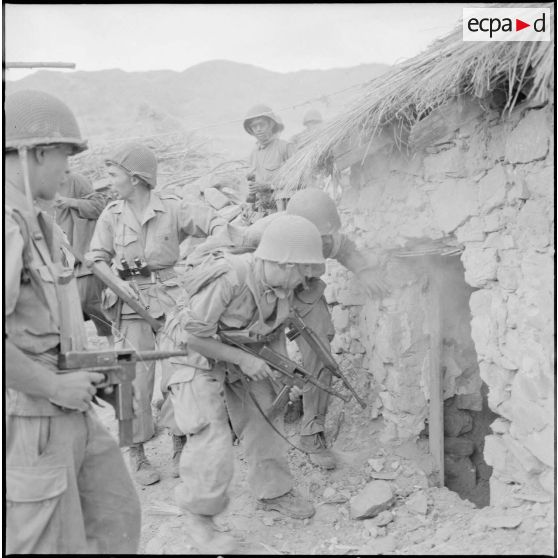 Des soldats armés se postent devant l'entrée en fumée d'une habitation.